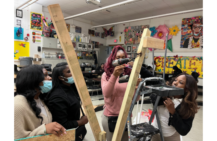 Five people collaborate on a creative construction project in a colorful classroom, using tools 